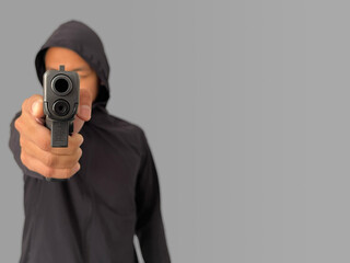 A man wearing a black hoodie Aiming a gun forward, focusing on a gun, simulating a shooting incident, an image showing signs of violence.
