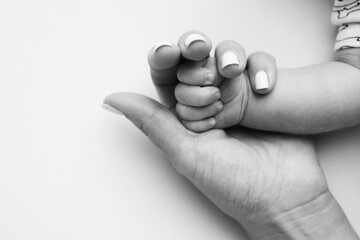 Parents' hands hold the fingers of a newborn baby. The hand of a mother and father close-up holds the fist of a newborn baby. Family health and medical care. Tiny fingers in a black and white photo.