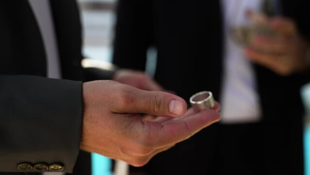 A groom in a tux playing with a silver wedding ring in his hand
