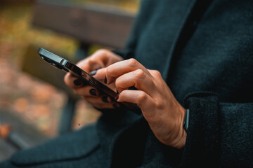 Woman writing a message on a smartphone while sitting on a park bench
