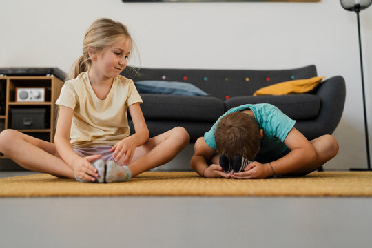 Full Body Of Adorable Boy And Girl In Casual Clothes Practicing Butterfly Yoga Pose On Carpet In Living Room At Home