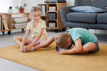 Full body of adorable boy and girl in casual clothes practicing Butterfly yoga pose on carpet in living room at home