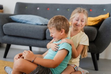 Cheerful little girl and boy in casual clothes playing together near sofa in living room at home