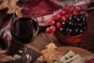 Glass of red wine served with blue cheese on dark wooden background. Autumn picnic with wine and cheese platter, fruits and dry leaves in rustic style
