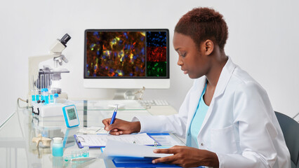 A woman in a lab coat writing on a piece of paper. African biologist checks records in scientific...