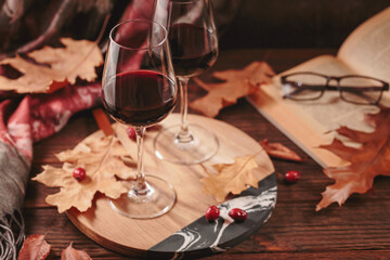 Two glasses of red wine served with fruits on dark wooden background. Autumn still life with wine, book and dry leaves in rustic style. Romantic sweater weather concept