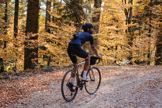 Fit male cyclist practicing on a gravel road in the forest during the autumn. He is riding a gravel bike. Autumn in Romania. Gravel biking adventure on beautiful forest trails. Sports motivation image