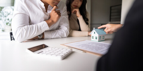 Young married couple sitting at table listening to realtor, real estate agent, loan broker or...