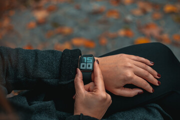 Young woman watching time on smart watch in a park. Time on the clock is 15-00. Girl in the autumn...