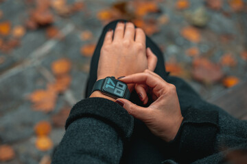 Young woman watching time on smart watch in a park. Time on the clock is 17-00. Girl in the autumn park. Blurred background. Full frame