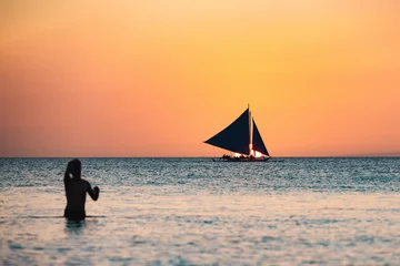 Runde Acrylglas Antireflex-Bilder Boracay Weißer Strand (Selective focus) Stunning view of a boat sailing during a beautiful sunset in the background and the silhouette of a blurred person swimming in the foreground. White Beach, Boracay, Philippines.