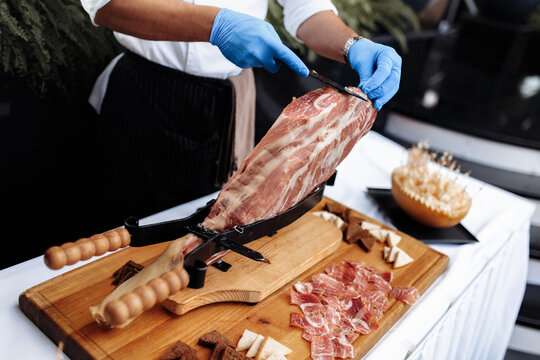 Side view of a professional cutter carving slices from a jamon. Mediterranean dish, gastronomic specialty.