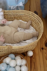 baby in beige knitted clothes lies in a wicker cradle basket