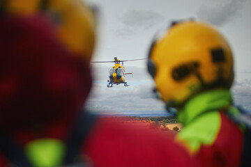 Rear view of paramedics wearing helmets as they looking at the approaching helicopter of emergency...