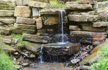 Close up of a small waterfall spilling over moss covered rocks in regional park. Handmade river...