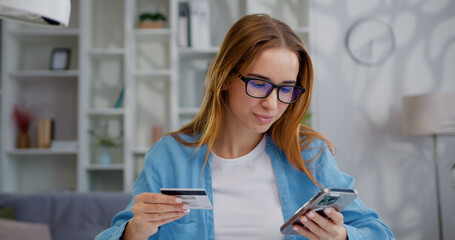 Businesswoman sitting at the table while doing online shopping through mobile phone at home. Girl holding credit card and mobile phone for payment purchase on web with secure banking service app