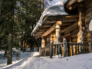 Porch of a wooden log house in a forest, covered by deep, thick snow