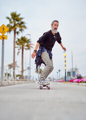 mature man white beard skateboarding on the street 	