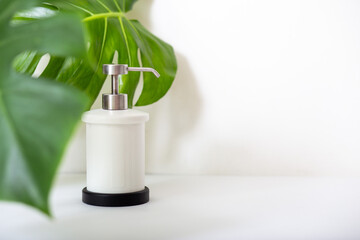 shower gel or liquid soap in a white bottle with a dispenser and green plant leaves on a white background with copy space