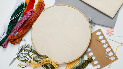 Embroidery set fot stitching. Beige cotton cloth in embroidery hoop on white background with fabric, colorful threads, scissors and needls. Indoor hobby concept with copy space, top view - obrazy, fototapety, plakaty