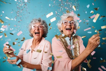 Obraz na płótnie Canvas diverse happy two senior women celebrating New Year at party with confetti on turquoise background. Female couple. Birthday celebration. 