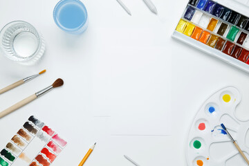 Watercolor and other artistic accessories on a white background. Artist's desk workplace. Top view, copy space, flatlay