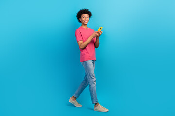 Full size photo of handsome young male walking hold telephone share post wear trendy pink outfit isolated on blue color background