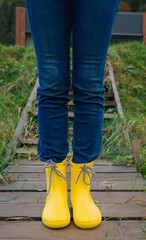 Yellow rubber boots on wet grass background. Walking in the rain. Walking in countryside in waterproof footwear. Bright yellow boots with blue jeans. Autumn fashion. Gumboots in countryside. - 672197278