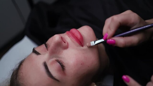 The permanent makeup artist applies the tone smoothing the contour of the lips.