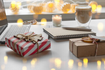 Notepad with a pen, laptop, coffee cup, wrapped gifts on a desk table. Winter Festive atmospheric mood. Preparation for Christmas. Business Holidays Concept. Freelancer's desktop during Xmas vacation