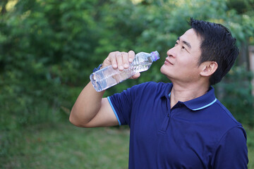 Handsome Asian man traveler holds bottle of drinking water to drink outdoors. Concept : Drinking...