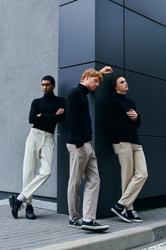 thoughtful multiracial men in black turtlenecks posing together with wall on background, fashion