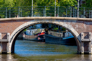 Summer cityscape, Canals of Amsterdam, Under view of brick bridge and railing, Still water and soft sunlight in the afternoon, Canal cruises is very famous activities, Tourist attraction, Netherlands.