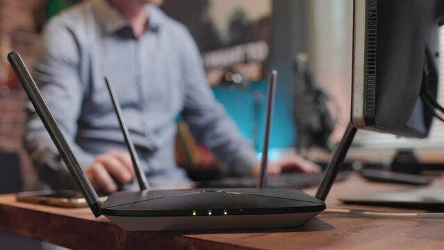 Router stands on the table and distributes Wi-Fi and the man uses this Internet and works at the computer and communicates on his mobile phone