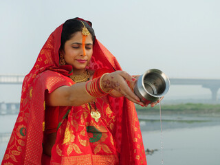 A traditionally dressed Indian woman in Chhath pooja attire is worshipping Lord Sun - Hindu...