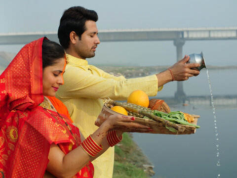 Traditionally dressed Indian couple worshiping God Sun - a celebration of Chhath Pooja festival  Bihari family  offering water. A man and a woman offering prasad to the Lord Sun on the occasion of ...