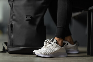 Black sports backpack and female legs in white sneakers