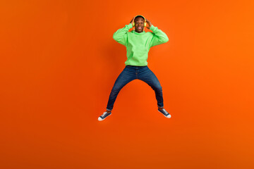 Fototapeta na wymiar Full size photo of funny flying man wear stylish sportswear jeans listen energetic playlist in headphones isolated on orange background