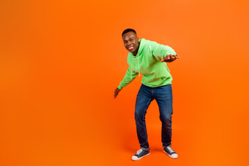 Fototapeta na wymiar Full size photo of pleasant optimistic man wear stylish sportswear jeans dancing at party having fun isolated on orange background