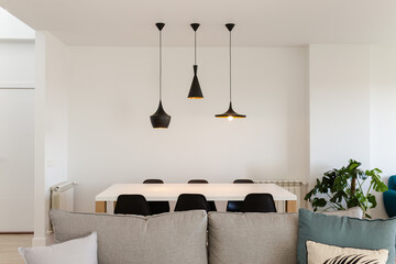 Front view of living room with white wooden table and six black chairs with three black metal lamps...