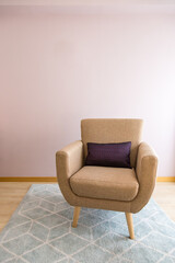 Fototapeta na wymiar One-seater armchair with cushion on light blue carpet, wooden floor and pastel pink wall. Natural light. Concept of empty chair, minimalism, solitude, listening space. Copy space