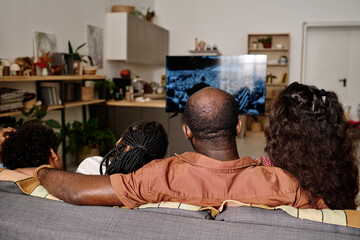 Black family watching recorded speech of Martin Luther King Jr on tv, view from the back