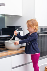 A little girl kneads the dough in a bowl