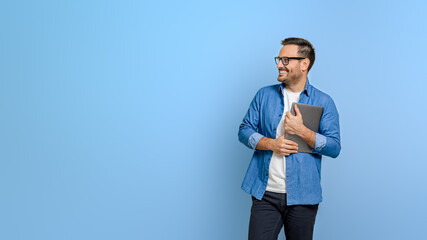 Smiling male professional holding digital tablet and looking away pensively over blue background - 672213455