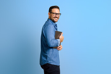 Side view of happy young male entrepreneur in eyeglasses holding digital tablet over blue background