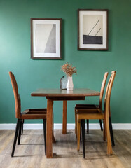 Wooden dining table and chairs against green wall with frames. Scandinavian, mid-century interior design of modern dining room.