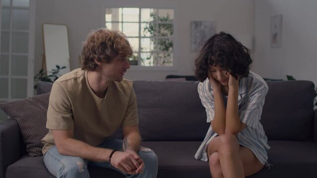 Young Caucasian man explaining himself to woman with black curls looking distressed listening to him