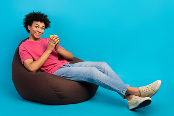 Full body photo of handsome young male sit brown beanbag hold coffee mug dressed stylish pink clothes isolated on blue color background