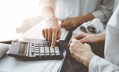 Woman accountant using a calculator and laptop computer while counting taxes for a client. Business...
