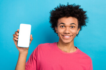 Photo of toothy beaming man with perming coiffure wear pink t-shirt demonstrate smartphone touchscreen isolated on blue color background